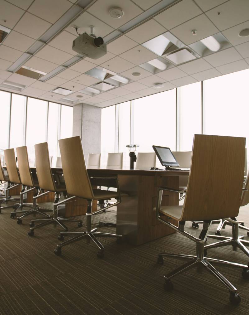 Modern conference room with a long table, chairs, and large windows showing an overcast sky